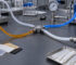 Laboratory bench with interconnected clear and colored tubing, metal fittings, and a pressure gauge in the background.