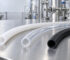 Three flexible tubing hoses—white, clear, and black—lie on a stainless steel bench in a processing facility.